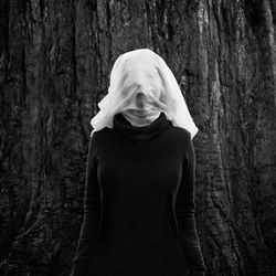 Woman with face covered standing against tree trunk 
