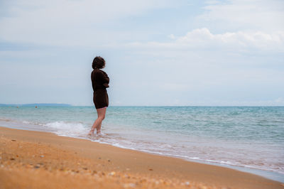 Rear view of woman standing at beach against sky