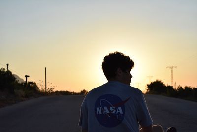 Rear view of man standing on road against sky during sunset