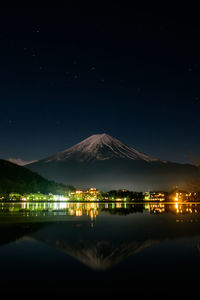 Scenic view of lake by illuminated mountains against sky at night