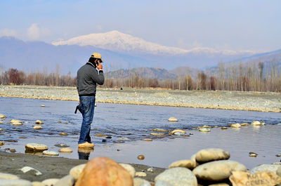 Rear view of man standing on field by lake during winter