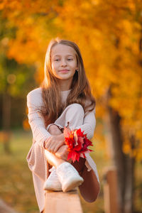 Smiling girl holding autumn leaf sitting outdoors