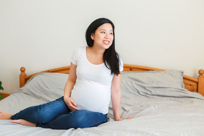 Pregnant woman sitting on bed at home