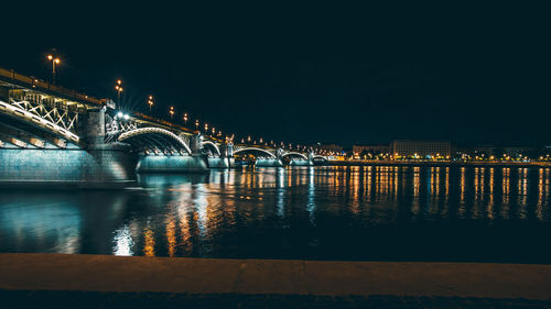 Illuminated arch bridge over river against clear sky at night