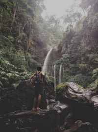 Full length rear view of man looking at waterfall in forest