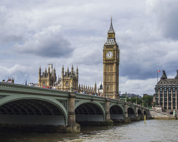 Westminster bridge over thames river against cloudy sky in city