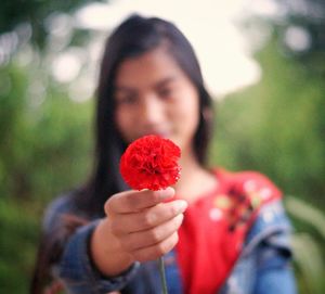 Close-up of woman hand holding red flower in park