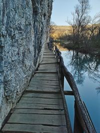 Wooden boardwalk by lake against sky