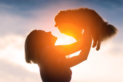 Low angle view of woman with arms raised against sky during sunset