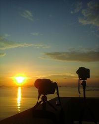 Silhouette man photographing sea against sky during sunset