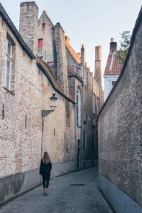 Rear view of woman walking on footpath amidst buildings