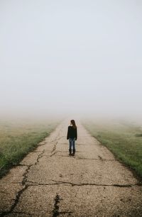 Rear view of girl standing on road during foggy weather