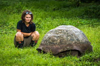 Woman looking at giant tortoise on field