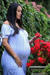 Beautiful hispanic woman expecting a baby, touching a flower in a public garden person