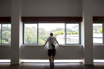 Full length rear view of woman standing by window