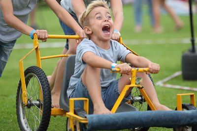 Midsection of sisters pushing cheerful brother sitting on vehicle