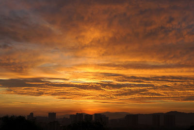 Silhouette buildings against dramatic sky during sunset