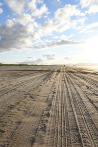 Tire tracks on sandy beach against partly clouded sky