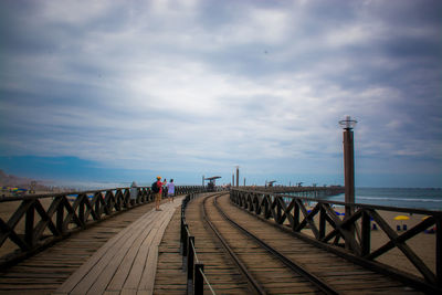 People on bridge by pier over sea against sky