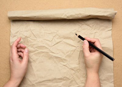 Empty torn sheet of brown craft paper and two hands with a black wooden pencil, wooden table, top v