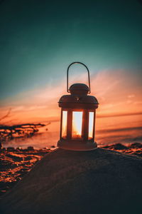 Close-up of old-fashioned lantern on rock at beach against sky during sunset