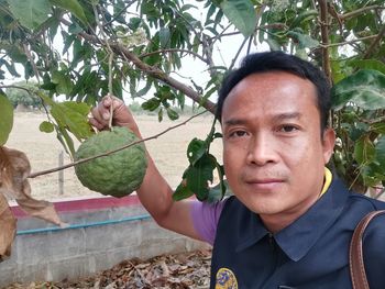 Portrait of man holding fruit on tree