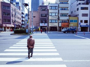 Woman crossing road against buildings in city