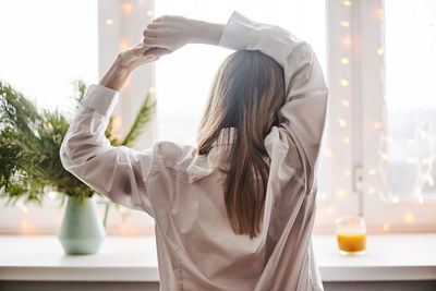 Rear view of woman looking through window at home