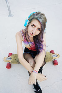 Portrait of young woman listening music while sitting on skateboard in park