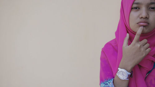 Portrait of young woman wearing pink hijab standing against beige background