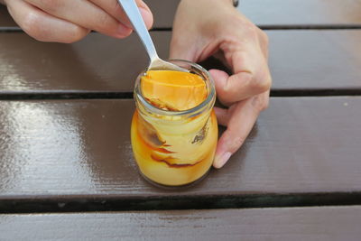 Midsection of person holding pudding in jar on table