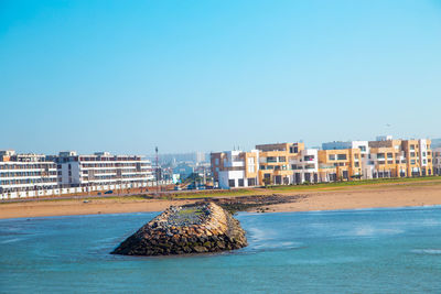 Buildings by sea against clear blue sky