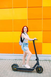 Young bright woman smiles and rides an electric scooter in the summer in city