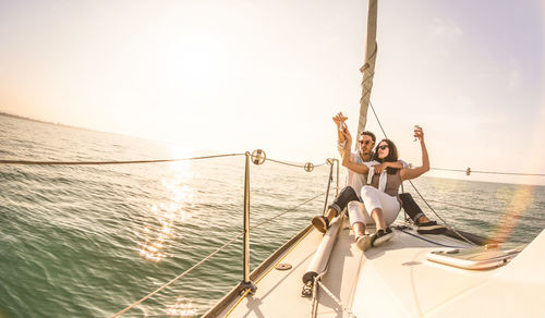 Young couple holding drink in glass on boat in sea against sky