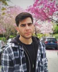 Portrait of young man standing against red flowering plants