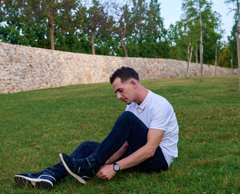 Side view of young man sitting on grassy field