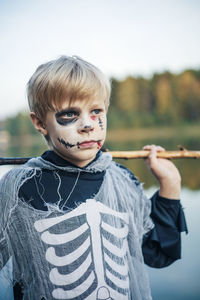 Happy halloween kid in carnival costume standing against the lake 