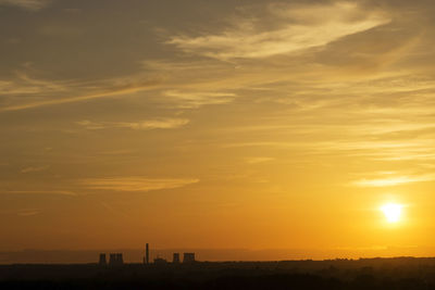 Silhouette factory against orange sky