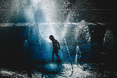 Side view of silhouette boy playing in fountain