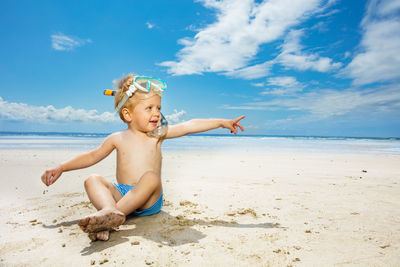 Rear view of shirtless boy playing at beach against sky