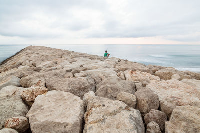 Man sitting on jetty over sea against sky