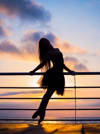 Silhouette woman dancing by railing against sea during sunset