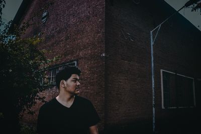 Portrait of young man looking away against building wall