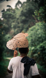 Rear view of man carrying dry leaf against trees