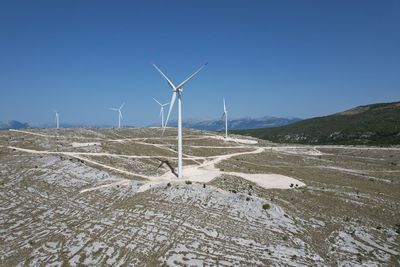 Wind turbines on land against clear blue sky