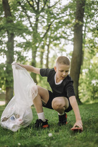 Full length of boy squatting and collecting garbage in bag on grass