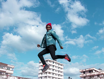 Low angle portrait of young man jumping against blue sky