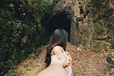 Cropped image of man holding woman hand against rock in forest