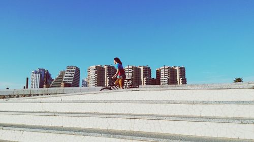 People walking in city against clear blue sky