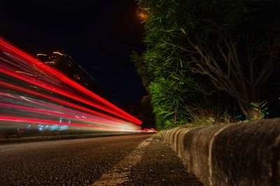 Light trails on road by trees at night